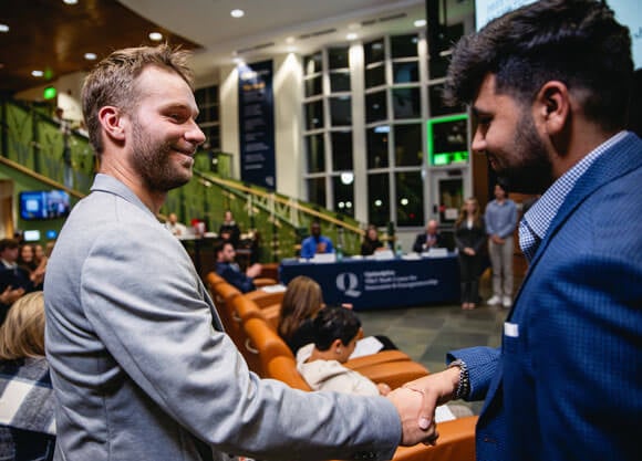 Two students in Quinnipiac Carl Hansen Student Center smiling and shaking hands