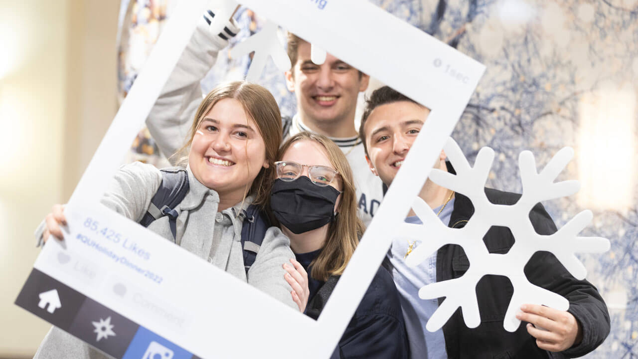 A group of students pose behind Instagram frame at undergraduate holiday dinner.