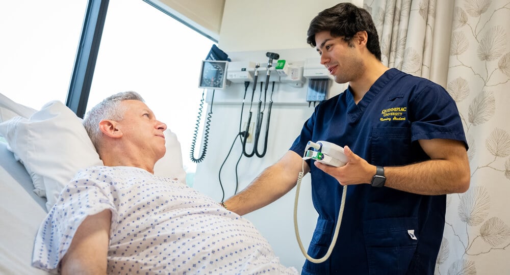 A nursing student tends to a patient in a hospital bed.