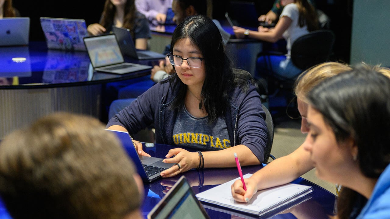 students sit around a table and work on their laptops