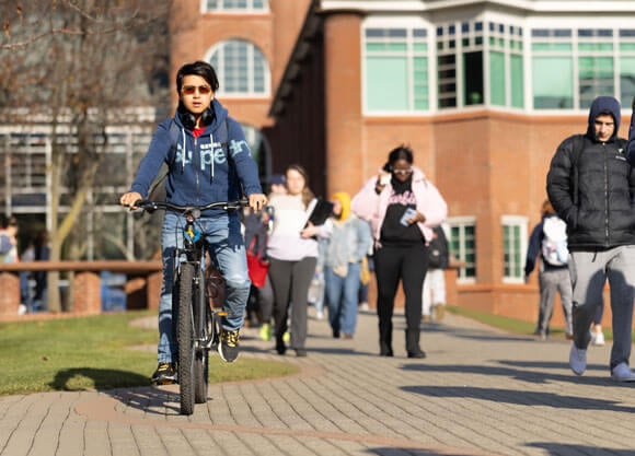 Student riding a bike in front of School of Communications and Engineering at Quinnipiac