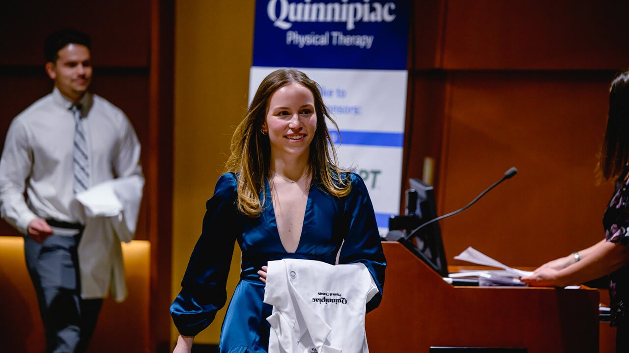 A student walking up to the stage holding their white coat.