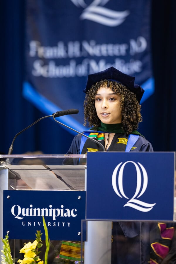 Madison Masters wears her graduation cap and gown and speaks at the microphone on the podium