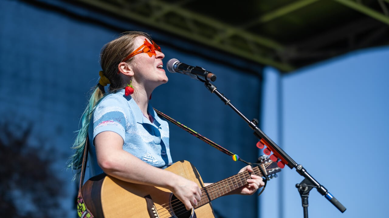 Person sings into the microphone wearing orange sunglasses