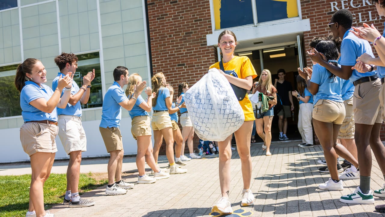 Student walks outside while carrying a white bag