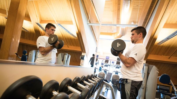 Student watching himself in the mirror lifting dumbbells in the York Hill gym