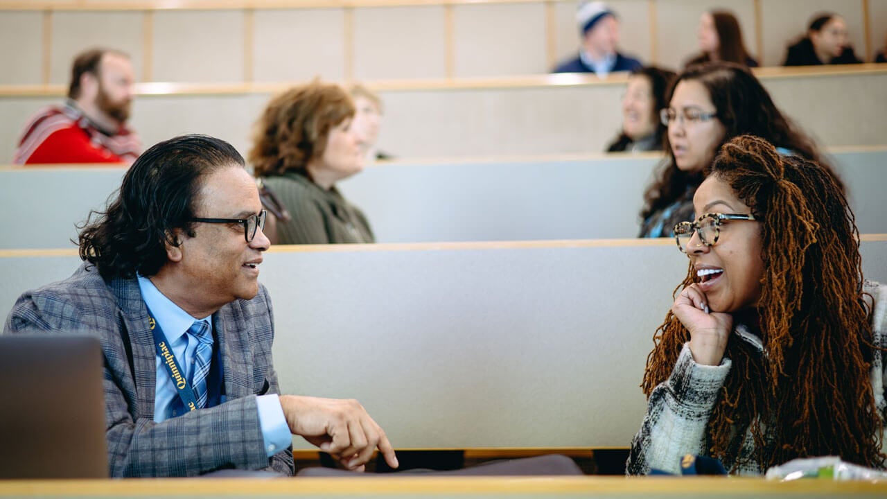 Two faculty members smile and talk to one another.