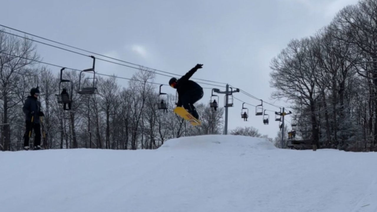 Student is in the air on a snowboard jump on a mountain