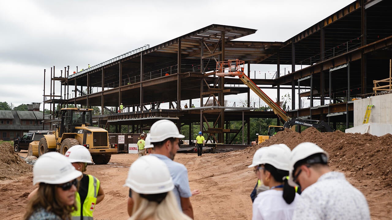 Staff and faculty talking with hard hats on in front of the construction site