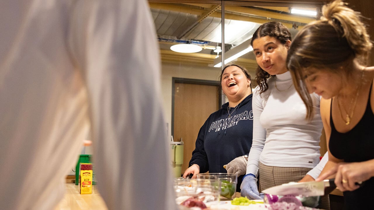 female student laughs at something off camera while another student chops an onion