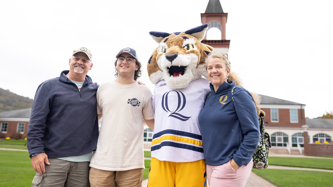 A student and his parents pose for a photo with Boomer on the Quinnipiac quad