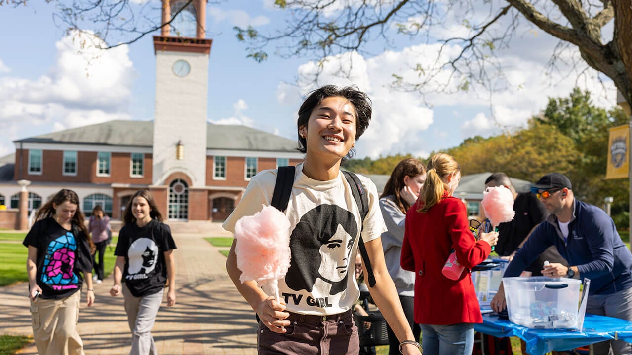 Students grins in front of the library holding pink cotton candy