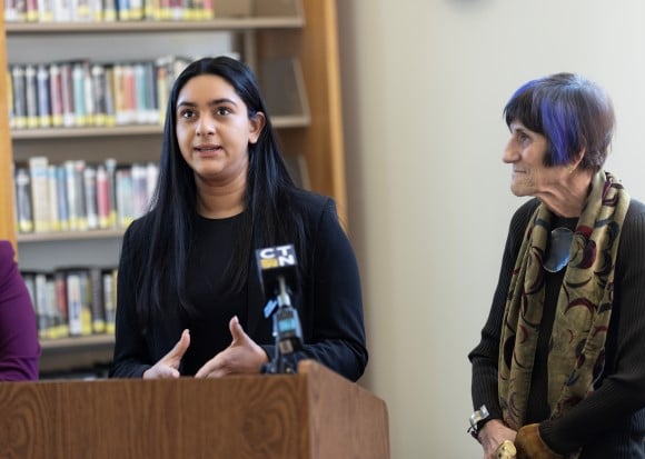 A woman speaks at a podium next to Congresswoman Rose DeLauro.