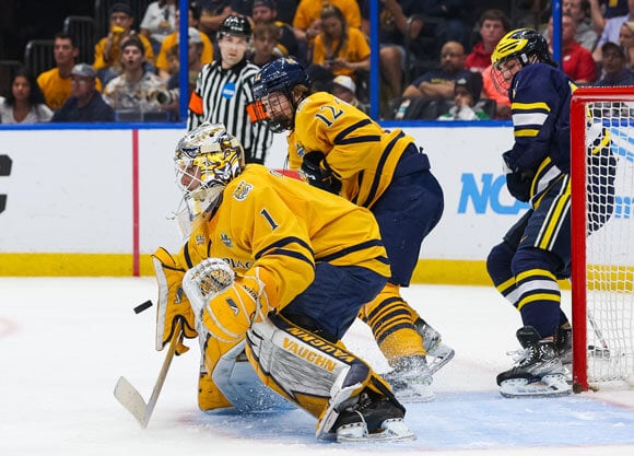 Yaniv Perets crouches in front of a goal on the ice.