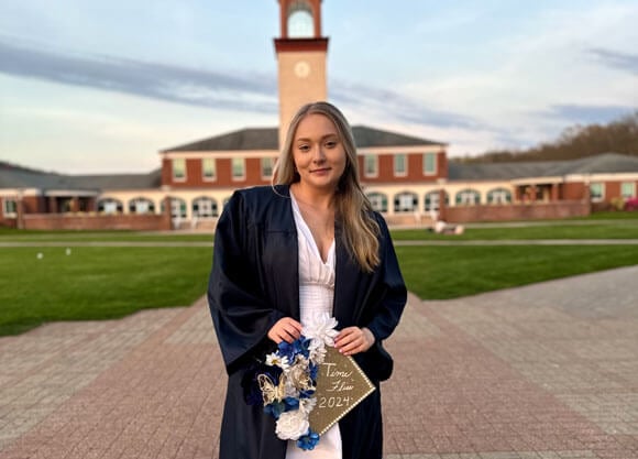 Lexi Pepe stands on the Quad holding graduation cap