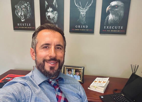 Altrin Elmazi selfie at his desk with inspiring words on wall behind him