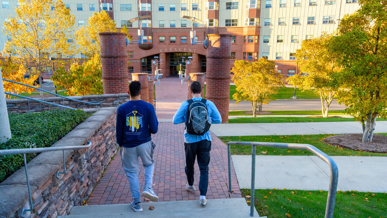 Two upper-class students walk toward the Crescent residence hall on a sunny fall day